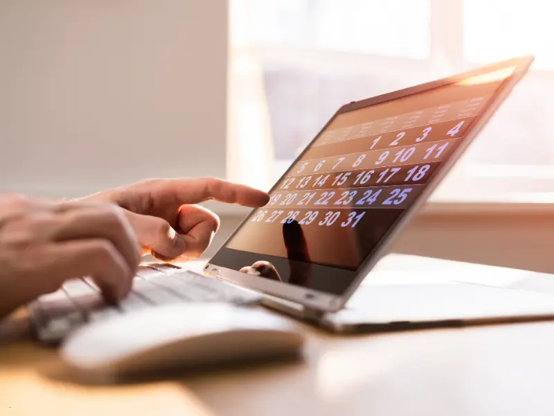 Smart calendar scheduling on a touchscreen laptop, with a person selecting a date in a sunlit workspace