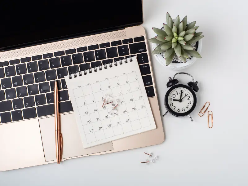 Open source scheduler visualized by a desktop calendar on a laptop with clock and office supplies